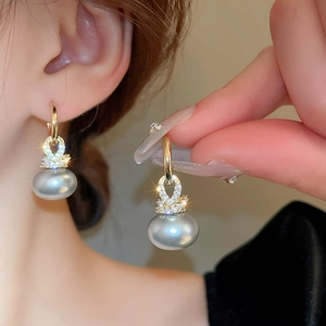 Détail d'une boucle d'oreille dorée avec perle grise et cristal de zircon scintillant