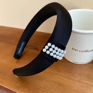 Elegant black satin padded headband with pearl accents on a wooden table with coffee cup