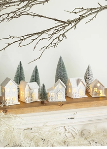 Close-up of white snow-covered LED wooden houses and miniature pine trees on mantel