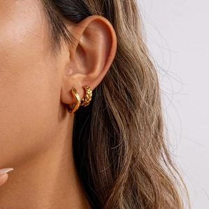 Detailed close-up of 18K gold stainless steel wave hoop earrings worn by a model