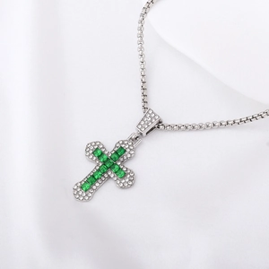 Macro shot of a silver cross pendant featuring a central green gemstone and micro-pavé crystals