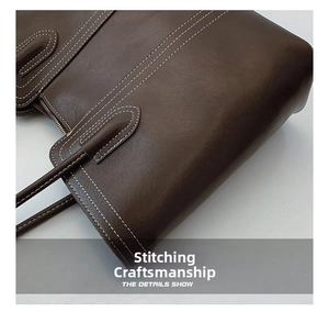 Detail of dark brown leather tote with decorative white contrast stitching and zip closure