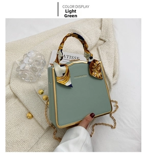 Detail of light green box bag with gold frame and silk scarf on the handle
