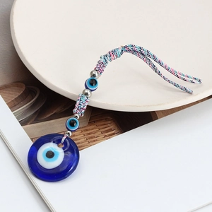 Blue Evil Eye glass charm with colorful braided rope on a minimalist wooden background