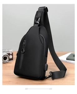 Detail of waterproof black crossbody bag with side USB charging port on a wooden desk