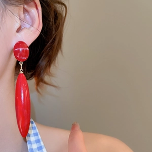 Detail of red acrylic drop earring with marble texture on model in blue shirt