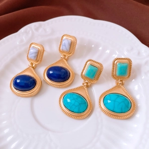 Detail of vintage gold oval earrings with blue and turquoise stones on a white relief plate