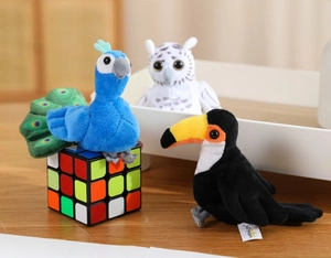 Three plush bird finger puppets including a peacock, owl, and toucan on a wooden desk