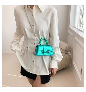 Green metallic mini hourglass bag with chain strap shown on a model in a modern room