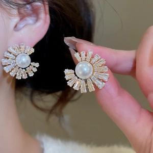 Macro shot of gold-plated pearl stud earrings with sparkling sunflower-shaped zircons