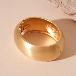 Detail of wide gold cuff bracelet featuring a brushed matte finish and hinged opening