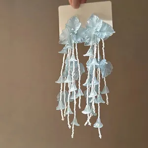 Close-up of light blue flower tassel earrings with layered translucent petals and beads