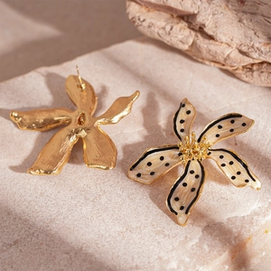 Détail de boucles d'oreilles fleur en émail avec pois noirs sur fond en pierre texturée