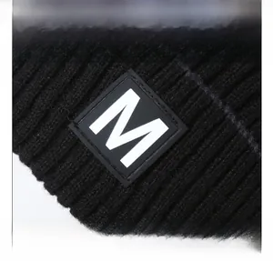 Detail of black ribbed knit beanie featuring a square patch with a white letter M