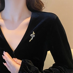 Close-up of golden dragon brooch with white pavé zircons on black velvet blazer