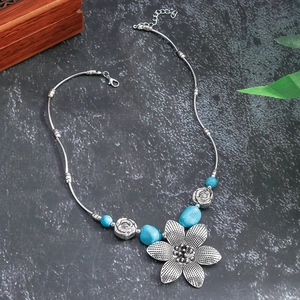 Macro shot of silver bohemian flower pendant with turquoise beads on stone surface