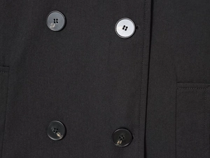 Detail of double-breasted buttons on a black short jacket with textured fabric