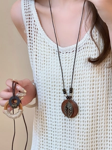 Detail of bohemian ethnic long necklace with hollow leaf pendant on white knit