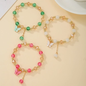 Détail de trois bracelets en perles de cristal avec breloques papillon en vert, crème et rose