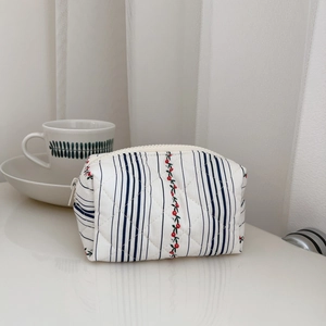 Detailed view of a quilted cotton pouch with blue stripes and cherry patterns on a desk