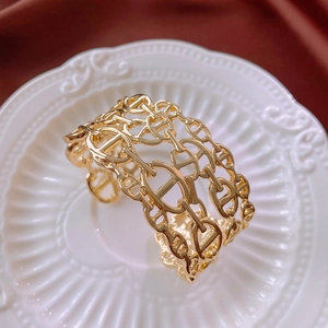 Detailed close-up of golden hollow three-layer chain link open cuff bracelet on white tray