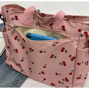 Detail of pink cherry print tote bag showing front zipper pocket with electronic device