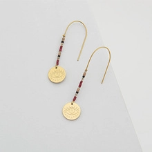 Detail of gold beaded earrings with colorful stones and engraved eye pattern pendant