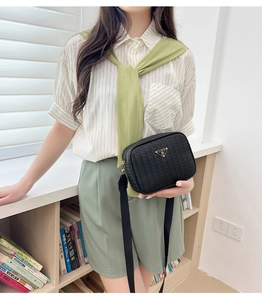 Detail of black woven texture crossbody camera bag with golden triangle metal logo plaque