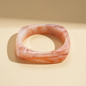 Détail macro d'un bracelet carré en résine acrylique avec texture marbrée rose et orange