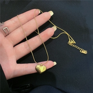 Golden stainless steel heart pendant necklace with snake chain held in hand