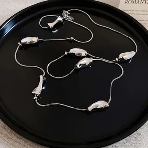 Irregular silver beads on long snake chain necklace over minimalist beige textured fabric