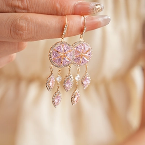 Close-up of vintage gold earrings with pink zircon, rhombus shape, and tassel leaf charms