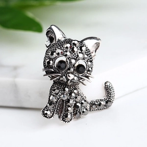 Vintage silver cat brooch with pavé rhinestones on a marble surface with greenery