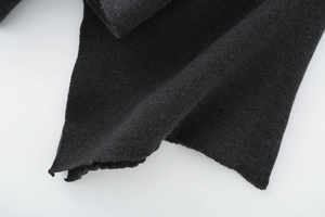 Detailed macro view of the black knit fabric texture and hem stitching on the cape coat