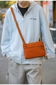 Outdoor street style shot of a casual orange nylon crossbody bag worn with a blue hoodie