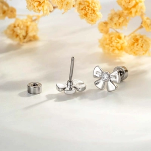 Silver bow stud earrings with clear gems and screw back closure on white surface