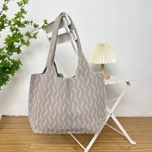 Detail of blue and beige wave pattern knit tote bag showing woven texture on a white chair