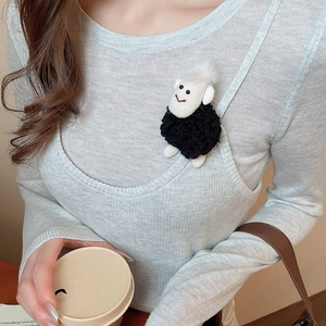Close-up of a cute plush sheep brooch pinned to a grey knit sweater on a model
