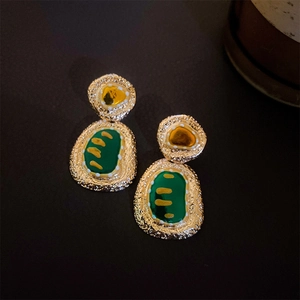 Detail of vintage gold earrings with textured metallic finish and green enamel accents