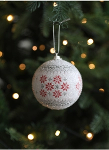 Close-up of white glitter Christmas ball with red snowflakes hanging on a green tree
