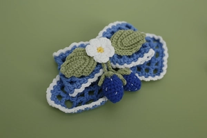 Detailed view of hand-knitted hair clip featuring blue strawberry and white lace flower