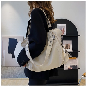Detail of a large cream tote bag showing thickness and metal rivet strap on a model