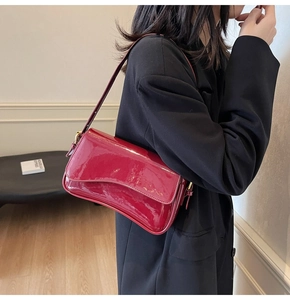 Close-up of wine red patent leather shoulder bag with glossy finish and gold metal buckle