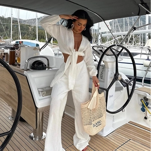 Détail d'un haut noué blanc et d'un pantalon large taille haute sur un yacht de luxe