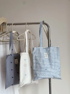 Three canvas tote bags with blue stripes, checkers, and bow embroidery on hangers