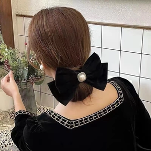 Detail of a large black velvet bow hair clip with a centered pearl on an elegant model
