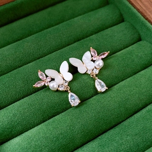 Detail of gold butterfly earrings with pink zircons and drop pendants on green velvet