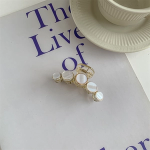 Detail of elegant mother-of-pearl hair claw clip with golden trim on magazine background