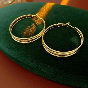 Dettaglio di orecchini a cerchio dorati multistrato con trama a rombi su velluto verde