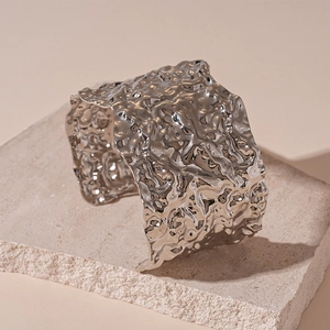 Macro shot of silver wide cuff bracelet with irregular lava texture on stone slab